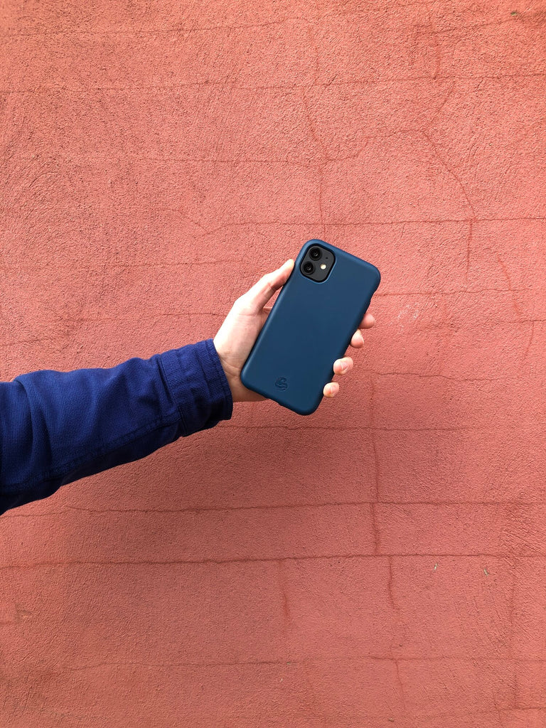 A hand holding a smartphone against an orange wall
