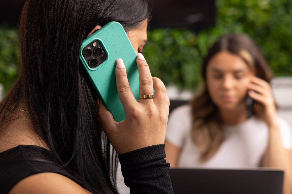 A lady holding a phone protected by a Wave Case phone case to her ear while sat at work in an office