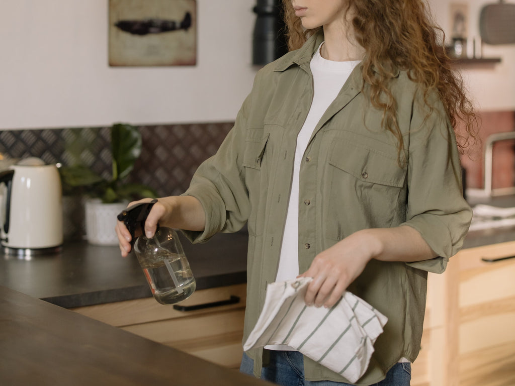 A lady using a spray bottle and cloth to clean in a kitchen