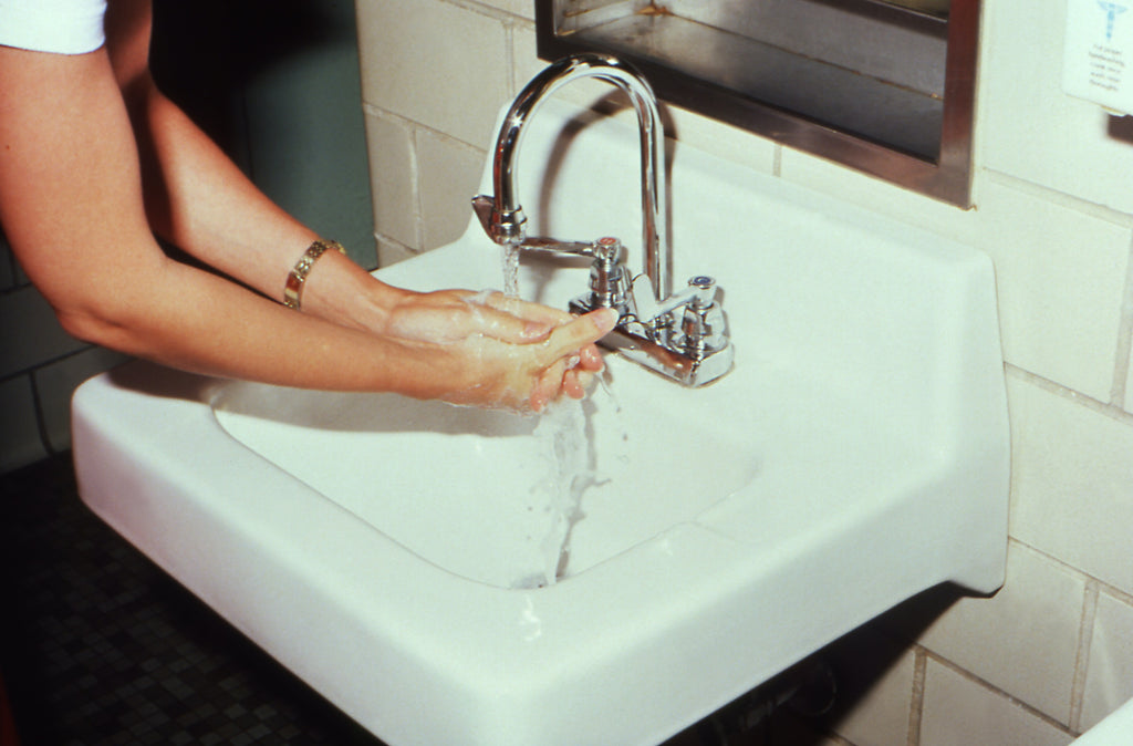 A person washing their hands in running water at a sink