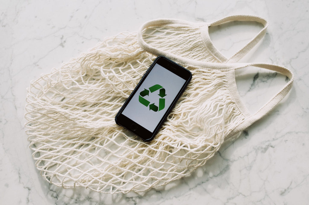 Smartphone displaying the recycle logo laid on top of a sustainable shopping bag